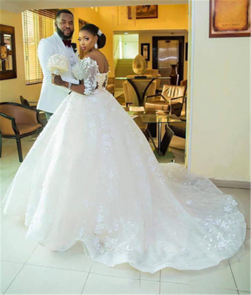 A voluminous white pregnant women princess wedding dress with intricate lace sleeves and a flowing train.