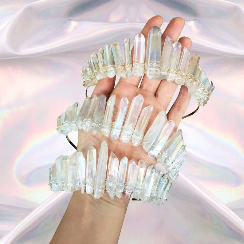 A hand holds three stacked iridescent quartz crown headband hair accessories made of translucent quartz crystal with delicate wire bindings.