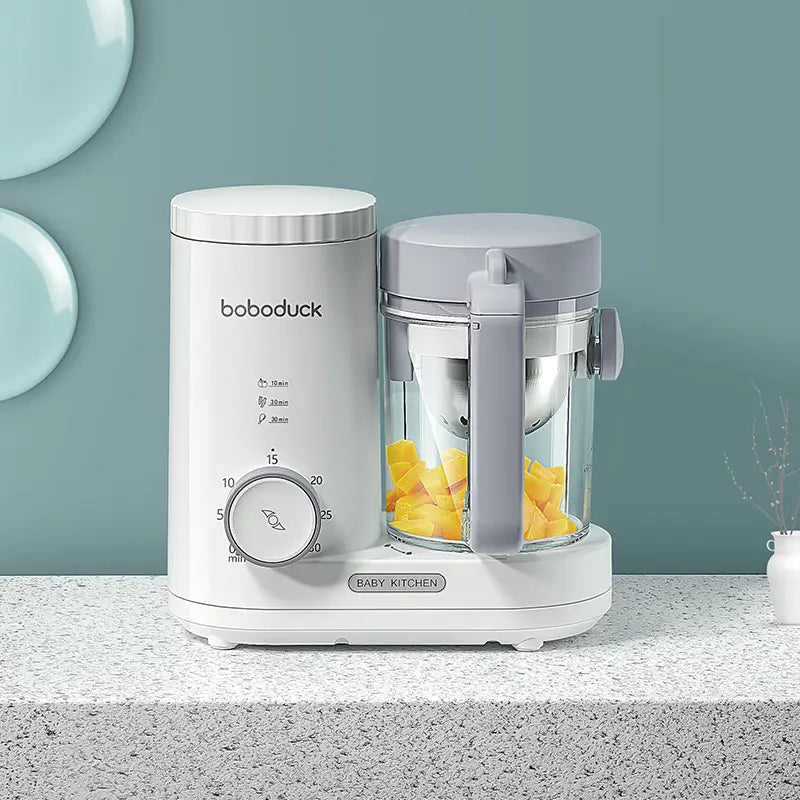 White and gray boboduck baby kitchen complementary food machine with a clear glass container filled with yellow fruit pieces for food machine cooking and mixing integrated small use.