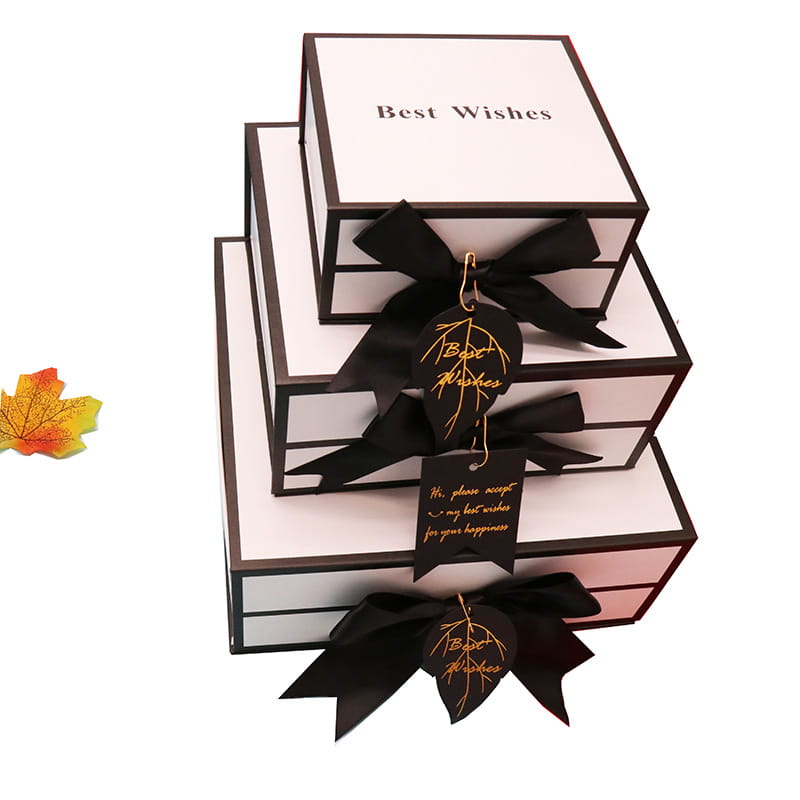 stacked white clamshell gift boxes with black satin bows and gold embossed best wishes tags designed as an elegant gift box for lipstick or other small items.