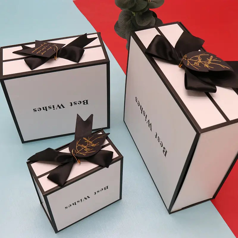 Elegant white clamshell gift box with black satin bow featuring black trim and gold foil lettering ideal for gift box lipstick packaging.
