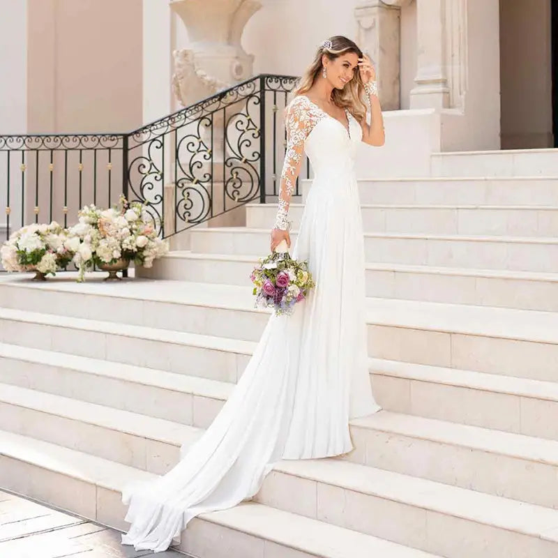 A flowing white wedding dress featuring delicate lace long sleeves and a sexy backless deep v-neckline.