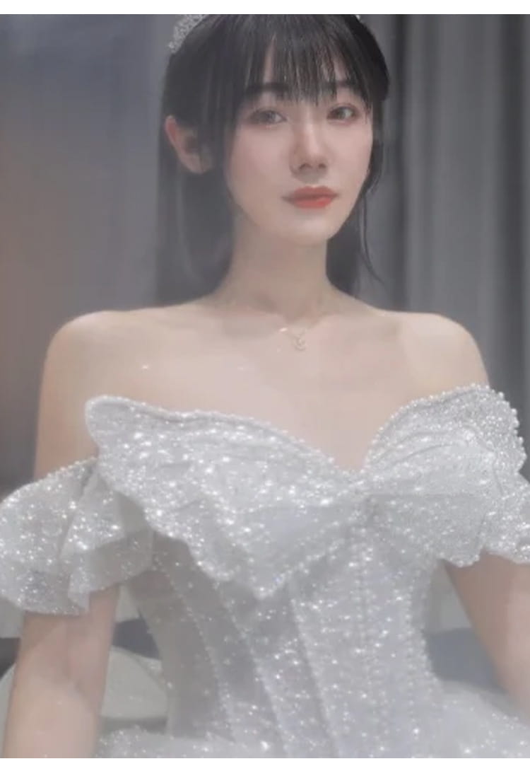 A shimmering white long trailing heavy industry wedding dress featuring an off-the-shoulder design with sparkling sequins and a voluminous ruffled bow at the bodice.