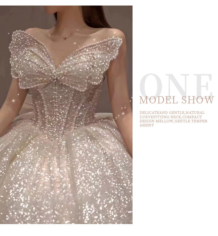 A shimmering off-white one-shoulder wedding dress features intricate beading and sequins with a delicate bow at the neckline and a long trailing heavy industry design.