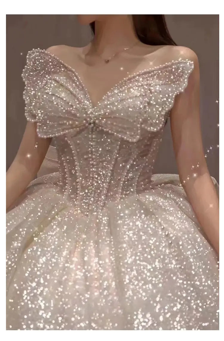 A shimmering white one-shoulder wedding dress with a sparkling butterfly-shaped sequin and pearl bodice paired with a voluminous tulle skirt in a long trailing heavy industry design.