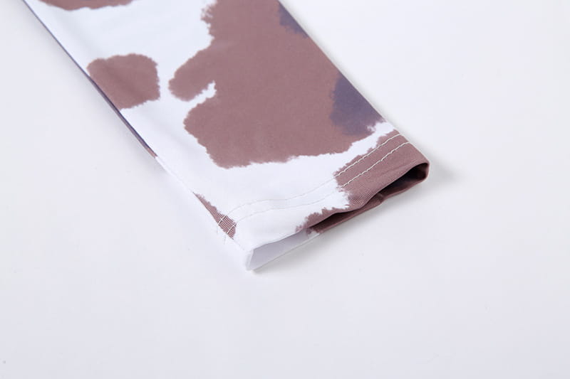 A close-up of a white and brown cow print women irregular hole maxi dress with long sleeves and neatly stitched cuffs.