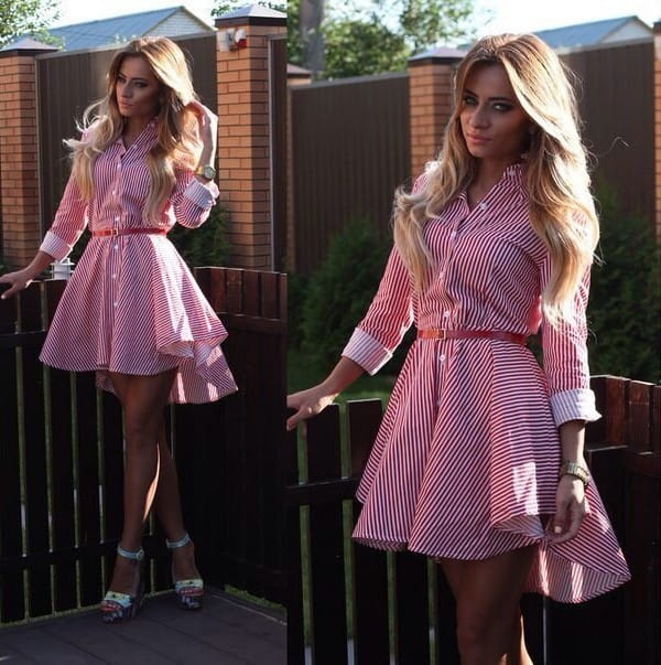 A pink and white vertically striped long sleeve shirt dress with a belted waist, three-quarter length sleeves, and an asymmetrical hemline for women.
