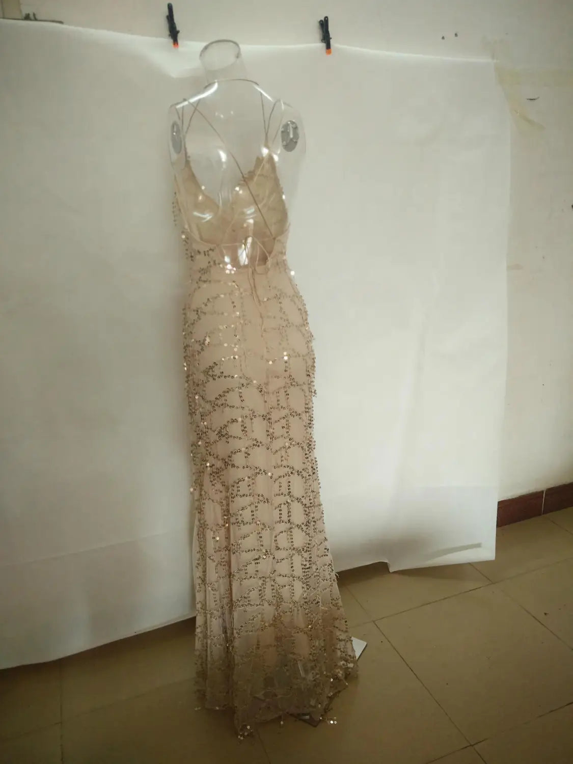 A shimmering champagne-colored strap sequin dress with a sexy halter strap, fitted silhouette, intricate beaded detailing, and a slit.