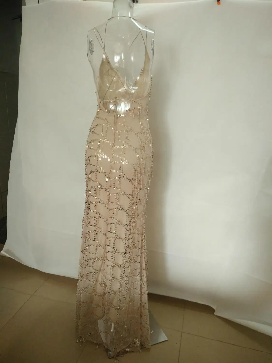 A shimmering champagne-colored gold v neck halter strap sequin dress with intricate beaded detailing and a fitted silhouette displayed on a mannequin.