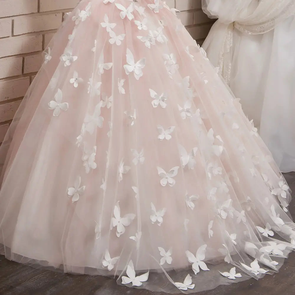 A delicate blush pink girls pengpeng skirt made of tulle fabric and adorned with scattered white butterfly appliqués.
