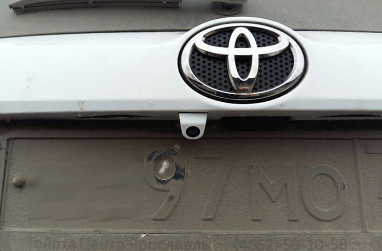 silver toyota emblem with a black perforated center mounted on the front grille of a white vehicle shown alongside a 4.3 inch led rear view mirror with reversing camera.