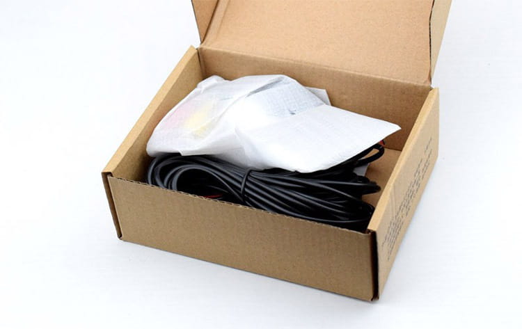 black coiled cable nestled in a cardboard box beside a white protective sleeve for a 4.3 inch led rear view mirror with reversing camera accessory