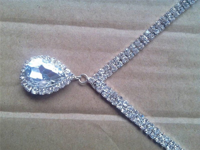 A silver v-shaped crystal bridal jewelry set featuring a sparkling silver rhinestone headpiece with a large teardrop-shaped crystal pendant and smaller surrounding crystals on a double-strand chain of clear stones.