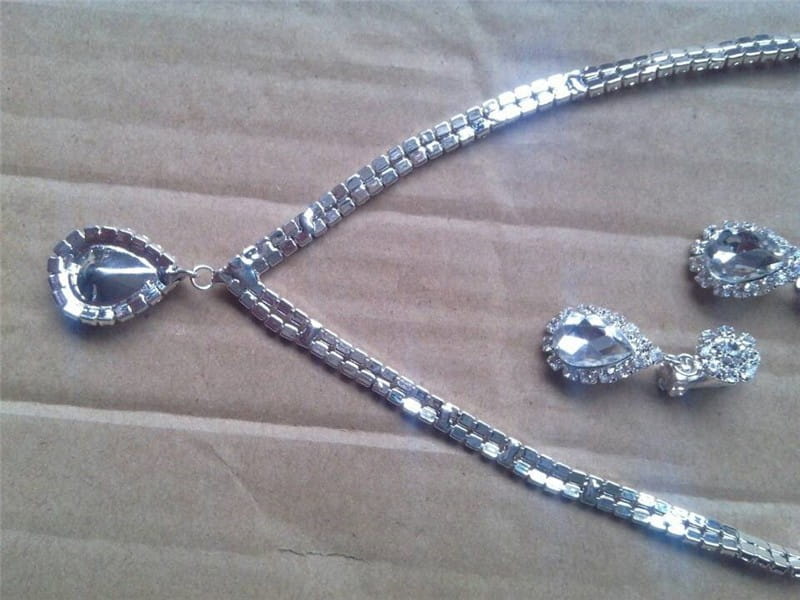 silver v-shaped crystal bridal jewelry set featuring a silver-toned necklace with pave-set teardrop pendant and matching earrings with sparkling rhinestones along the chain as an elegant bridal jewelry set.