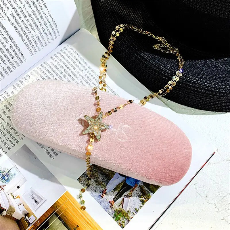 A delicate gold-toned starfish pendant necklace with sparkling rhinestones and dangling golden beads rests elegantly on a soft pink velvet eyeglass case showcasing the mso-font-pitch variable mso-font-signature design.