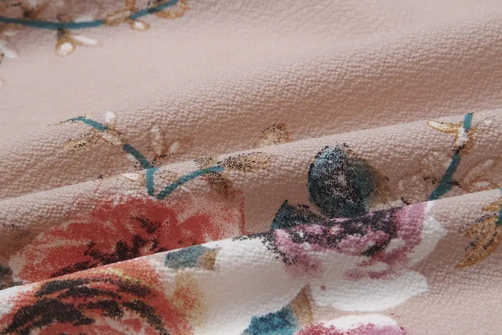 a soft blush-colored fabric with a delicate floral pattern in shades of red pink teal and gold featured on a boho style long off shoulder maxi dress for women