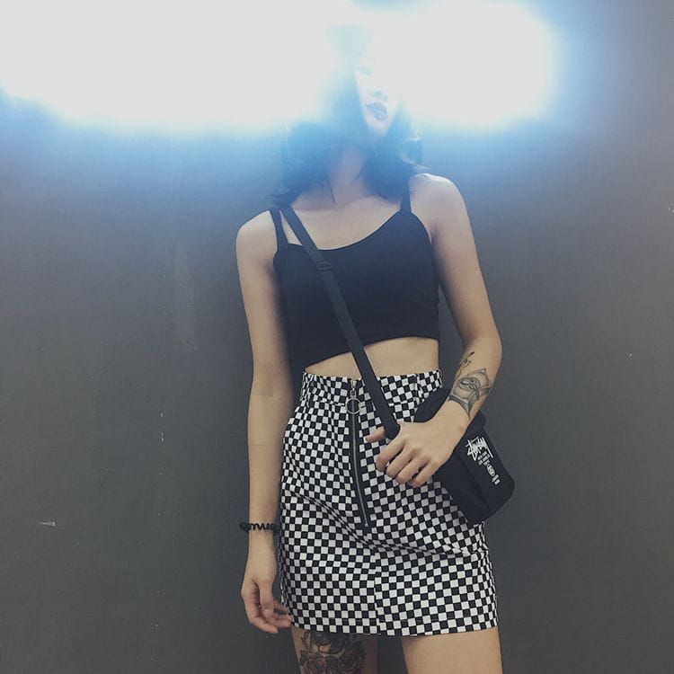 black crossbody bag with white graphic logo and zipper detail paired with a checkered mini skirt featuring variable mso-font-signature design elements