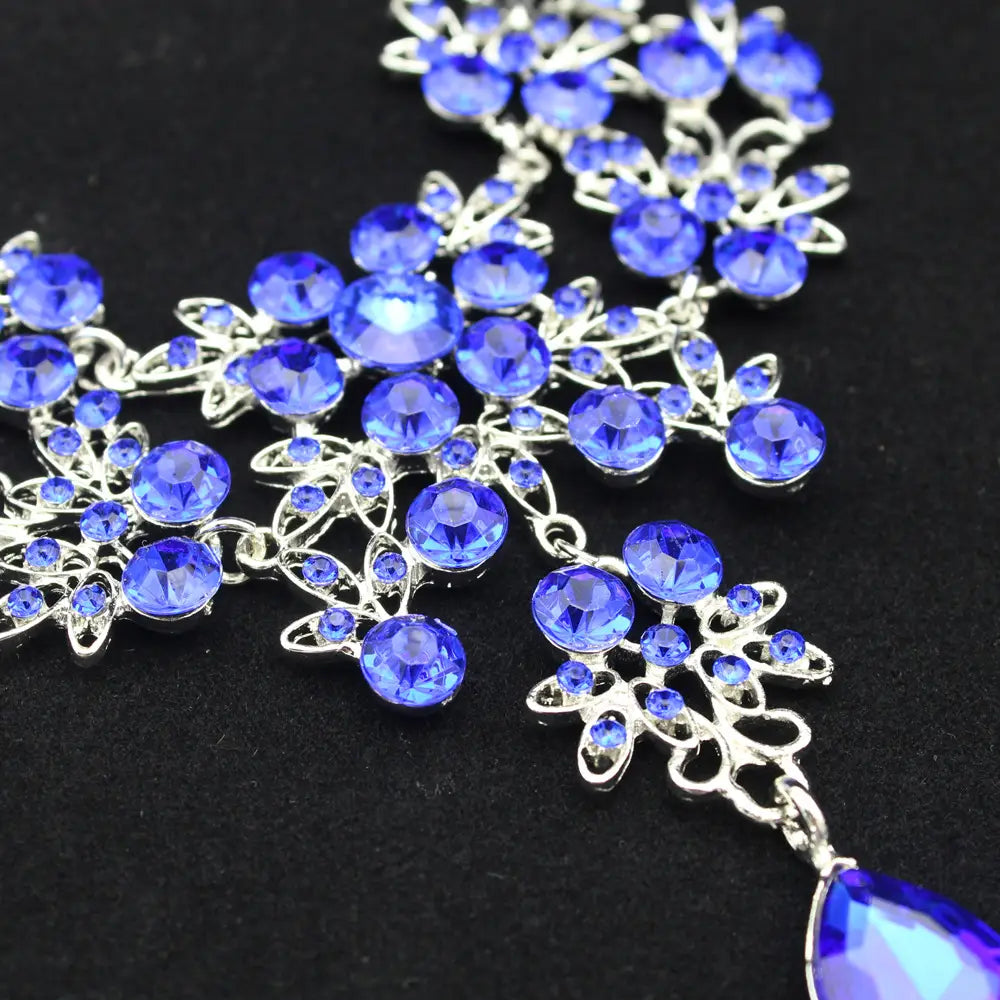 A sparkling blue crystal butterfly big water drop necklace with intricate silver-toned floral designs and a teardrop-shaped pendant in an earring set.