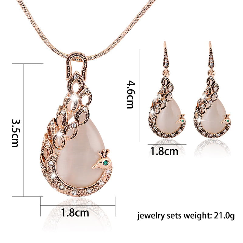 Rose gold peacock jewelry set featuring a pendant necklace and matching drop earrings with translucent pale pink jade-like stones, clear crystal accents, and a small green gemstone on the bird eye.