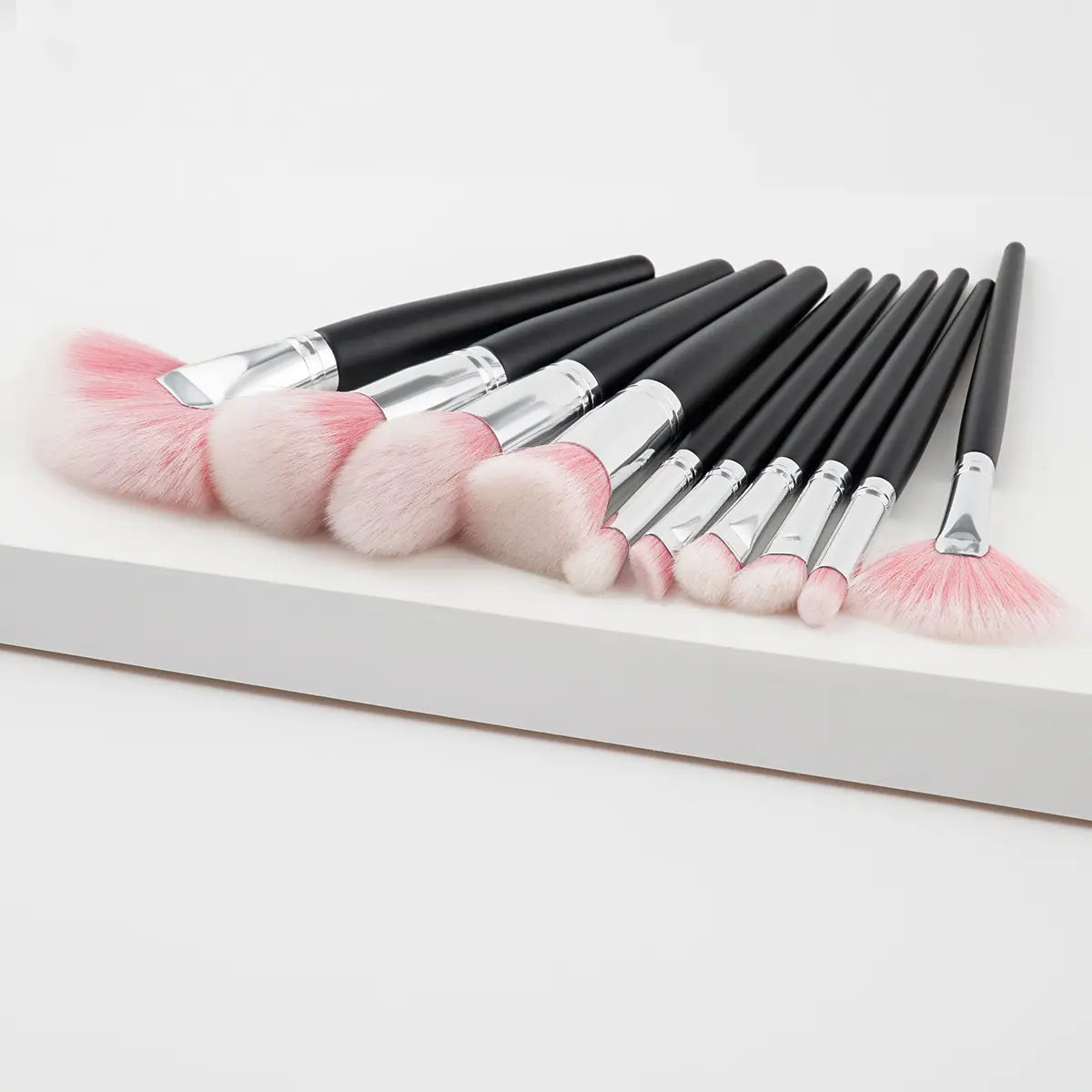 Set of ten black-handled makeup brushes with silver ferrules and soft pink bristles arranged neatly on a white surface from a 10 piece purple gradient makeup brush set.