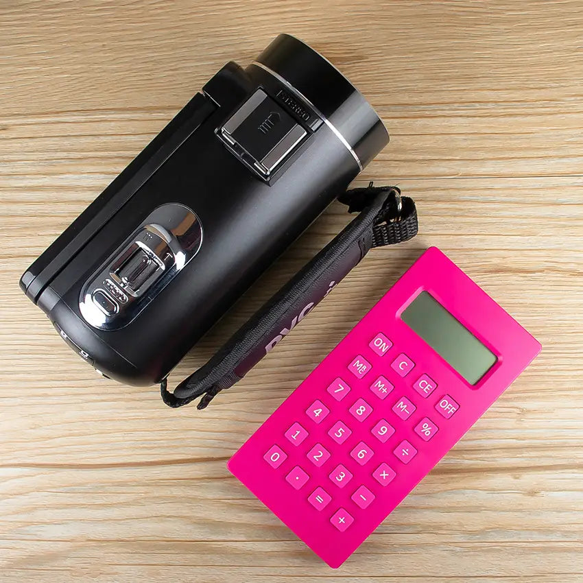black cylindrical digital camera with silver accents and wrist strap next to bright pink calculator showcasing royale essence lux hd digital camera with microphone and flip screen