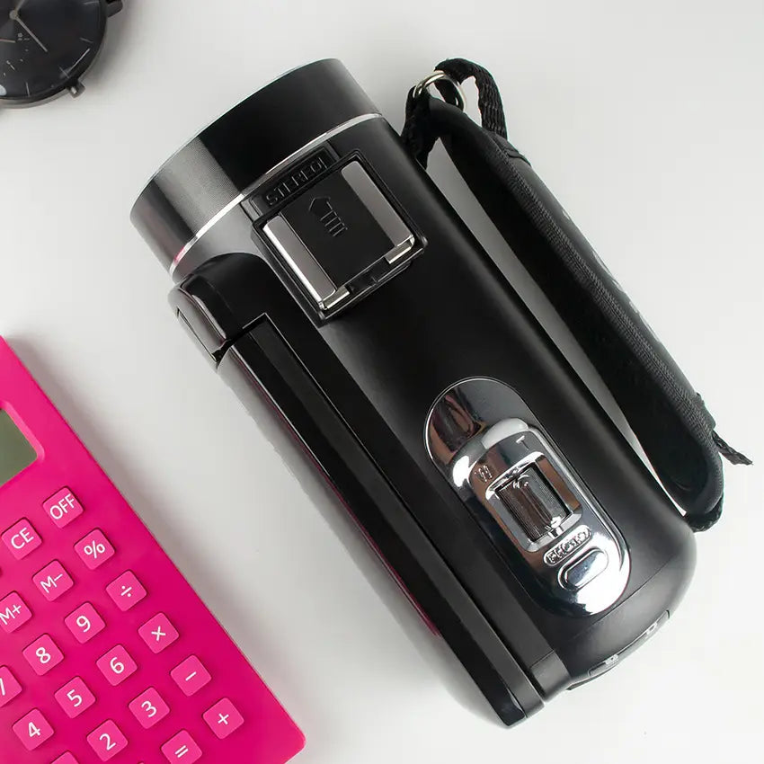 Black handheld HD digital camera with silver accents, microphone, flip screen, and wrist strap from Royale Essence Lux.