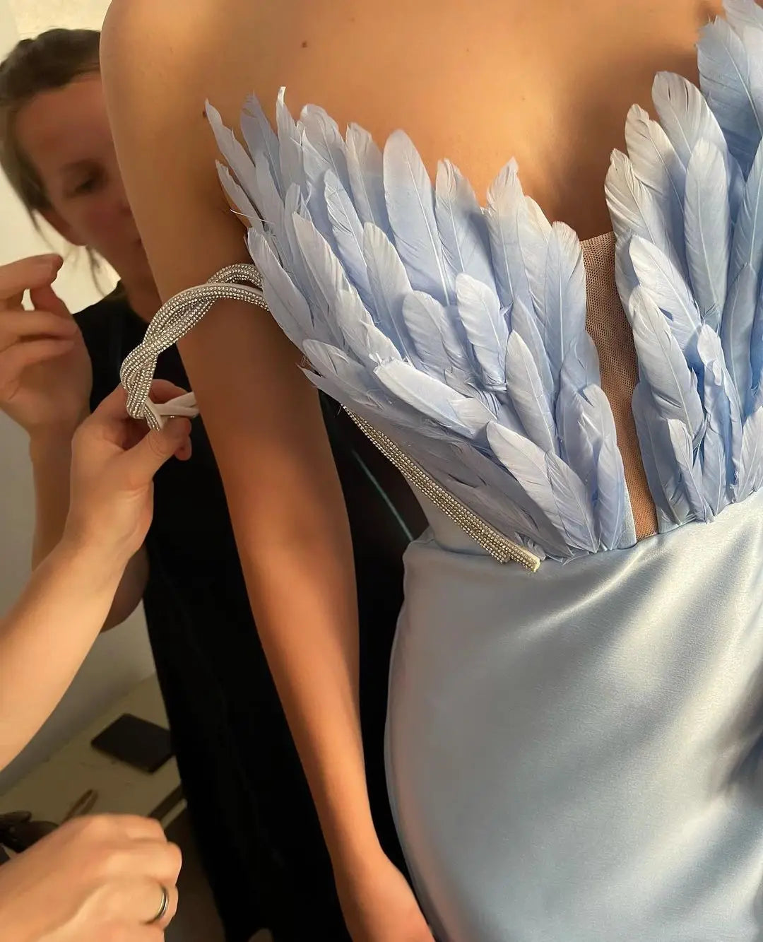 A light blue feathered corset top paired with a white satin skirt featuring feathers sweeping the floor in luxury women’s fashion.