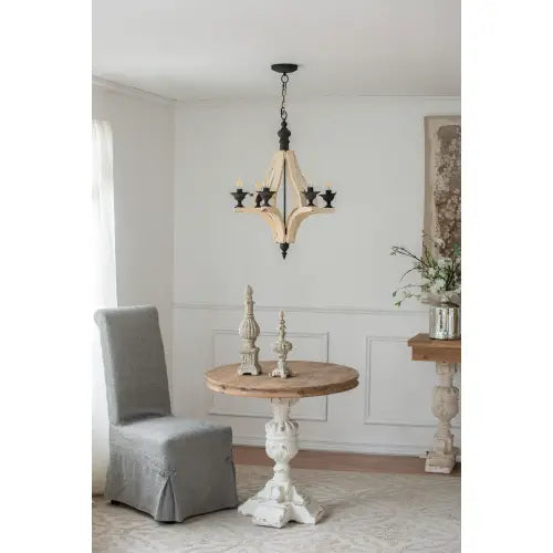 a rustic wooden table with a round top and ornate white-painted pedestal base beneath a light wood chandelier in a dining hall entrance