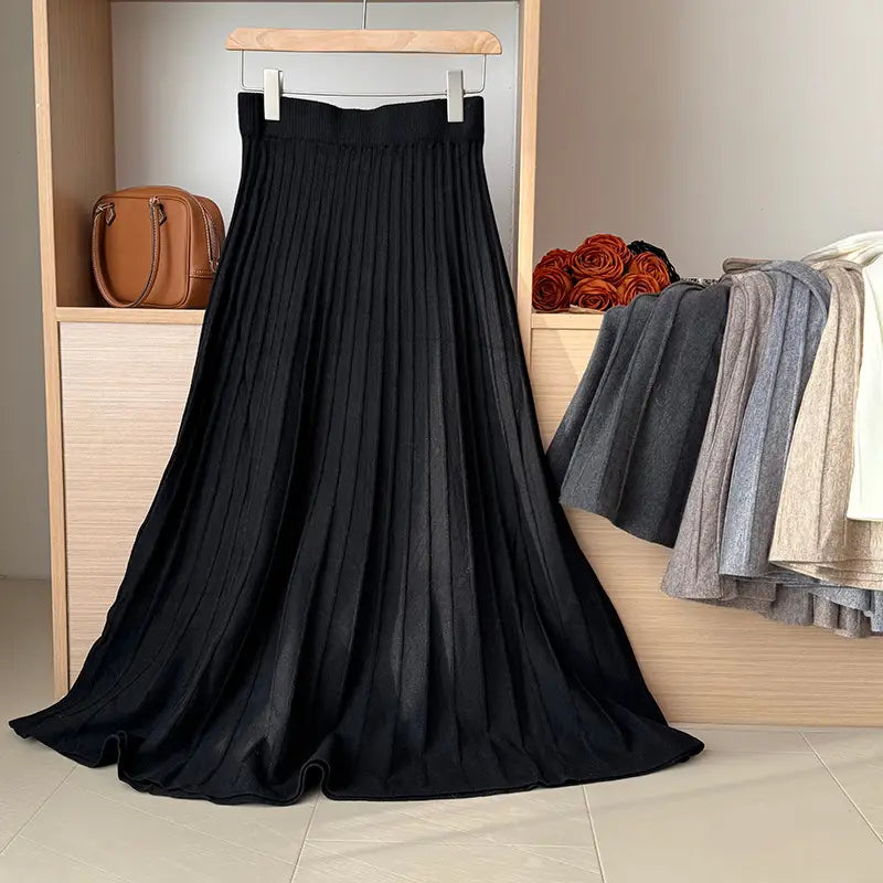 Black pleated midi skirt with korean elastic waist made of knitted fabric hanging on a wooden hanger.