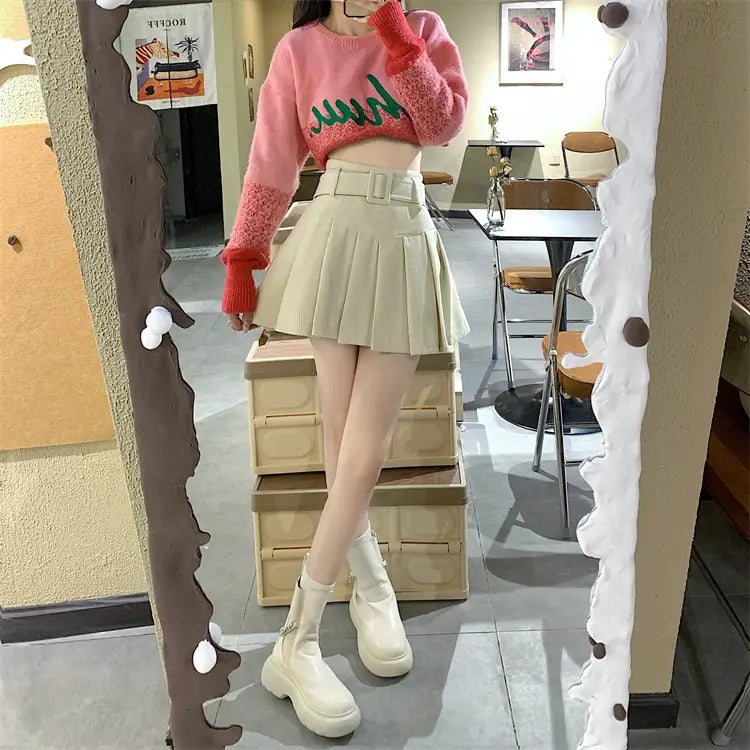 pink knit sweater with green embroidered design and red ribbed cuffs paired with brown belted corduroy half pleated skirt mini.