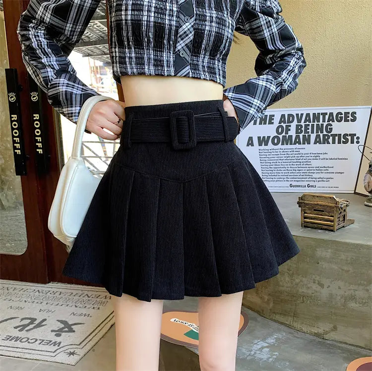 black corduroy half skirt pleated mini with a matching brown belt featuring a rectangular buckle.