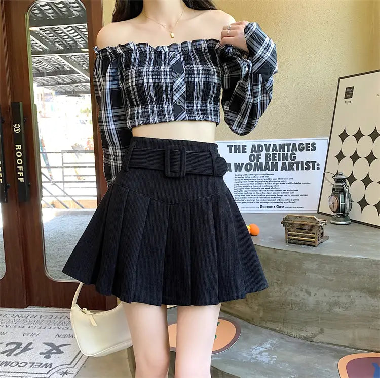 black pleated skirt with a wide belt featuring a rectangular buckle showcasing a corduroy half skirt pleated design.