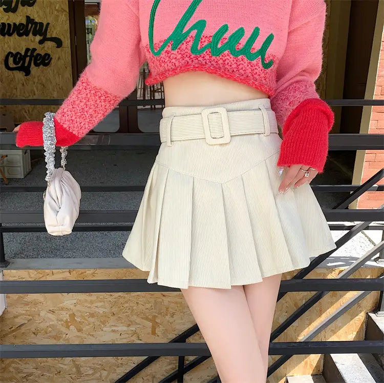 cream-colored corduroy half skirt pleated mini with a brown belted rectangular buckle for stylish wear.