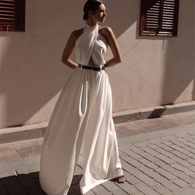 a flowing white sexy sleeveless halter maxi dress with a draped neckline, wide-leg silhouette, and cinched waist by a black belt, styled as a sleeveless halter backless jumpsuit.