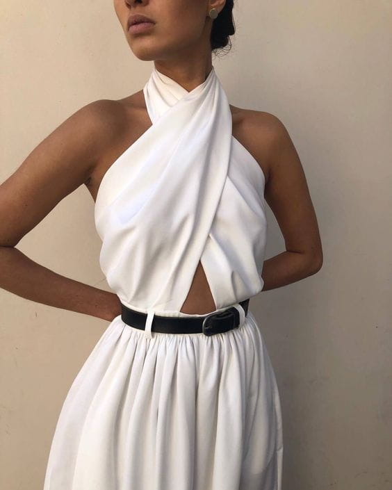 white sexy sleeveless halter jumpsuit with a draped asymmetrical neckline and black belt at the waist showcasing a sleeveless halter backless design.