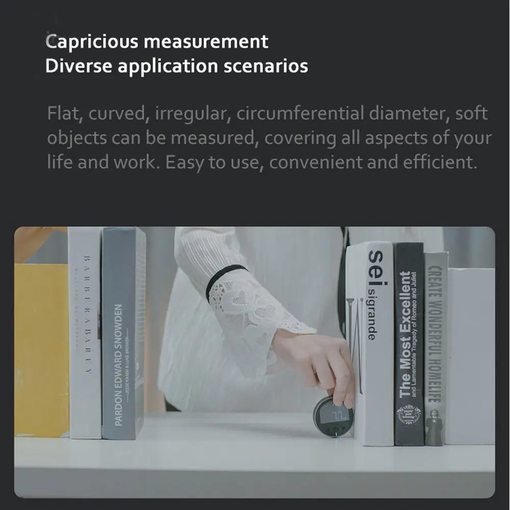 Black digital electronic measuring ruler with LCD display resting on a white surface between books for precise electronic measuring tasks