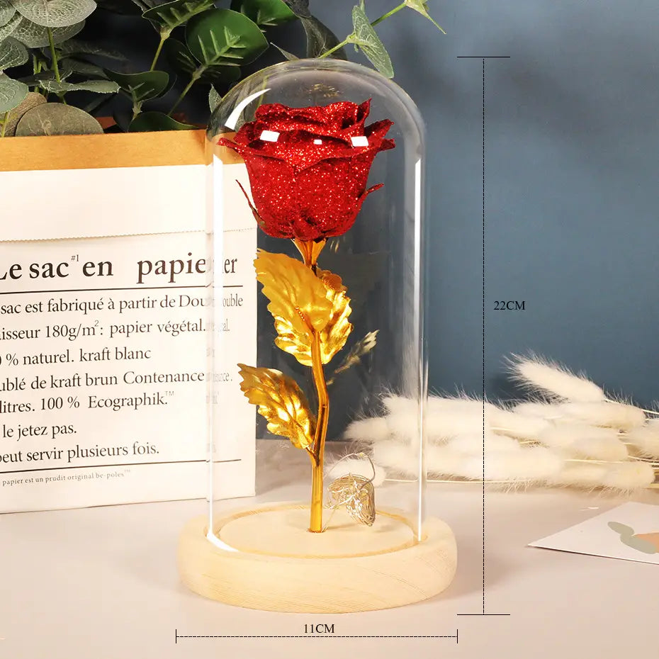 a glittering red eternal rose led with golden leaves and stem encased in a clear glass cover on a light wood base as a rose led light in a 5 pack