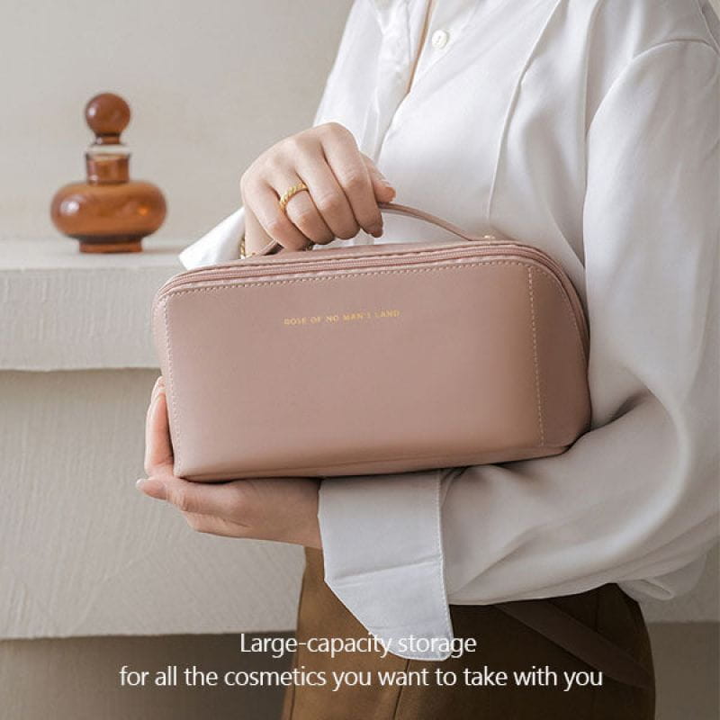 A soft blush pink leather travel cosmetic bag with large capacity, top handle, and subtle gold lettering on the front.