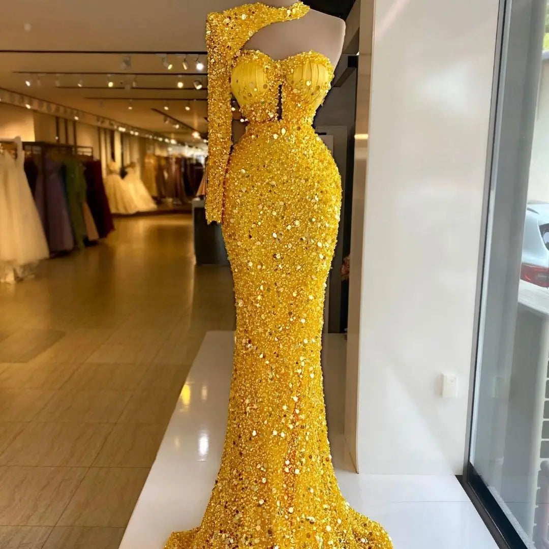 A dazzling gold sequined pearl embroidery lace asymmetric mermaid gown with a one-shoulder design and long sleeve displayed on a mannequin in a boutique setting.