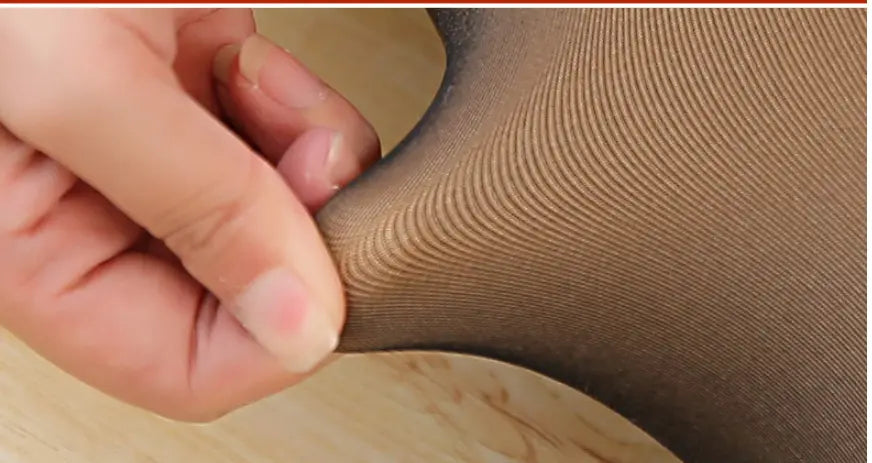 A close-up of a hand gently stretching sheer nude-colored adjustable maternity pantyhose tights with a subtle ribbed texture.