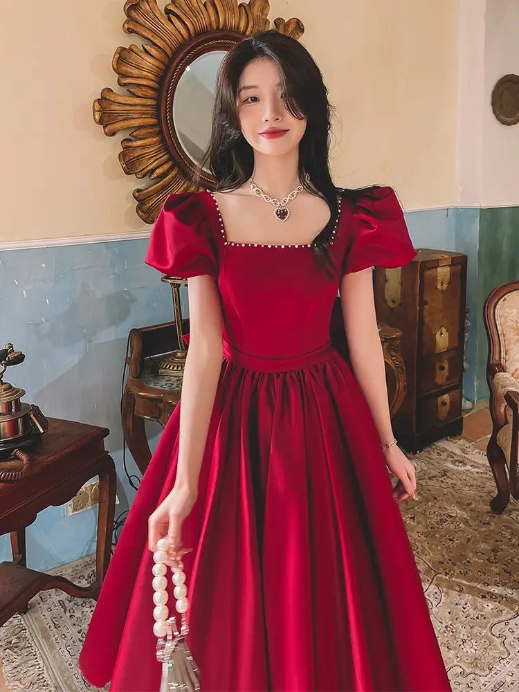 A rich wine red satin engagement dress featuring puffed short sleeves, a square neckline, and delicate beaded trim along the edges.