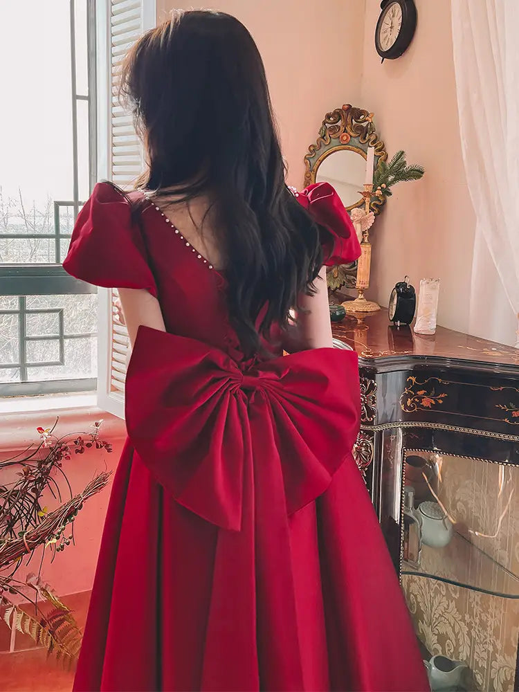 A vibrant winter wine red satin engagement dress with puffed short sleeves and a large bow at the back.