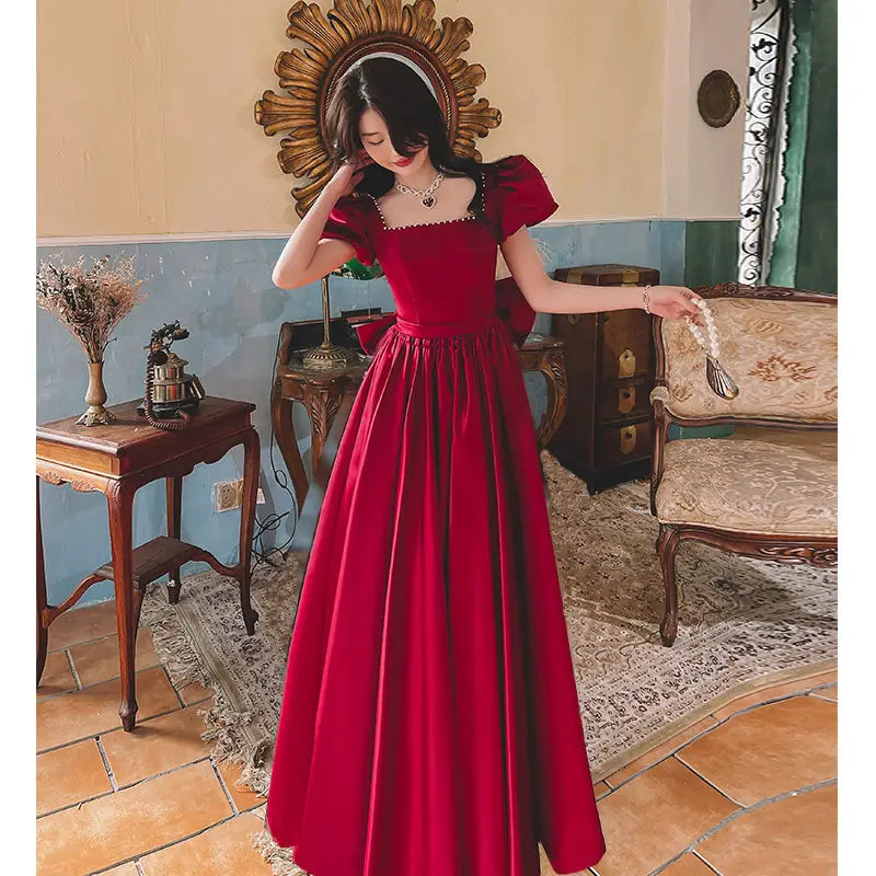 A winter wine red satin ball gown engagement dress featuring a square neckline, puffed short sleeves, and a fitted waist with a bow.