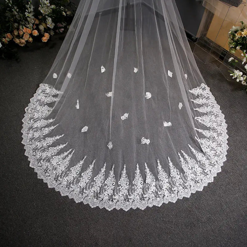 A delicate white lace wedding veil with intricate floral embroidery and scalloped edge featured in a lace wedding dress trailing floral bridal veil.