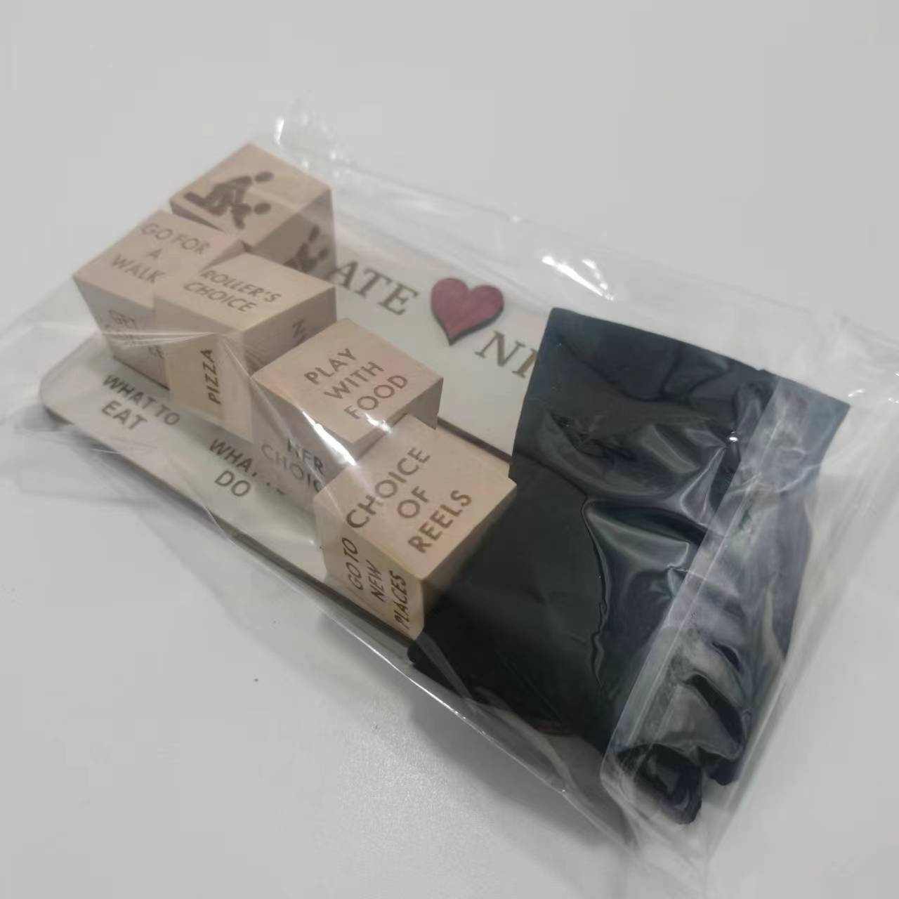 Set of wooden date night dice with engraved playful phrases packaged in a clear plastic bag alongside black fabric for a wooden date night game.