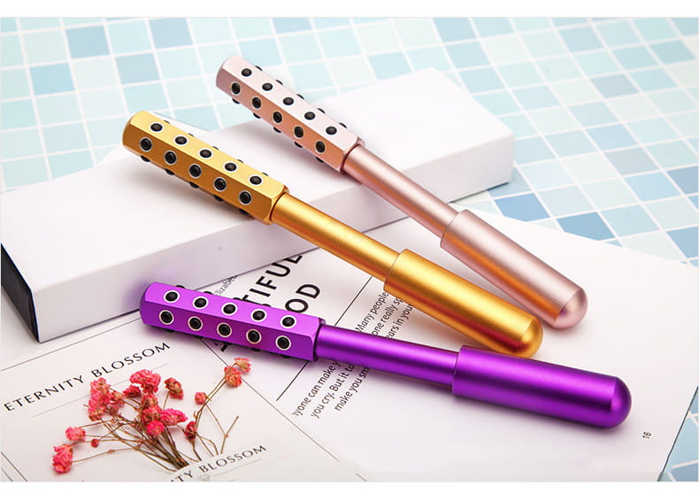 three metallic germanium beauty roller massage sticks in gold rose gold and purple with black circular indentations for facial massage and skincare.
