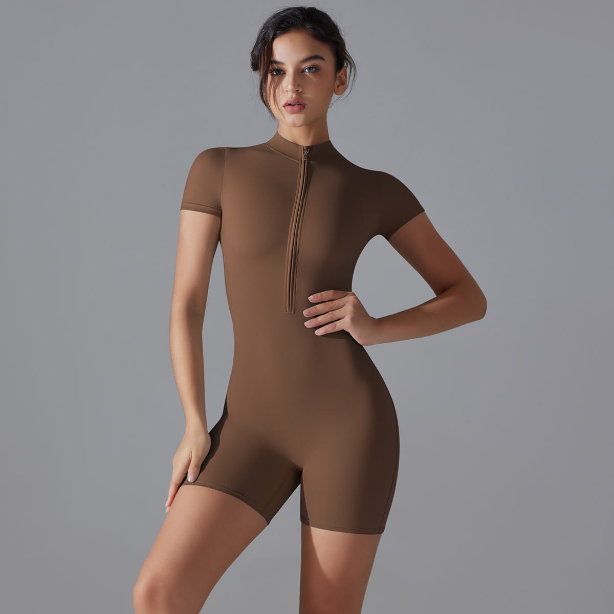A sleek brown one-piece athletic shorts jumpsuit yoga bodysuit with short sleeves and a high collar zipper designed for summer zipper convenience.