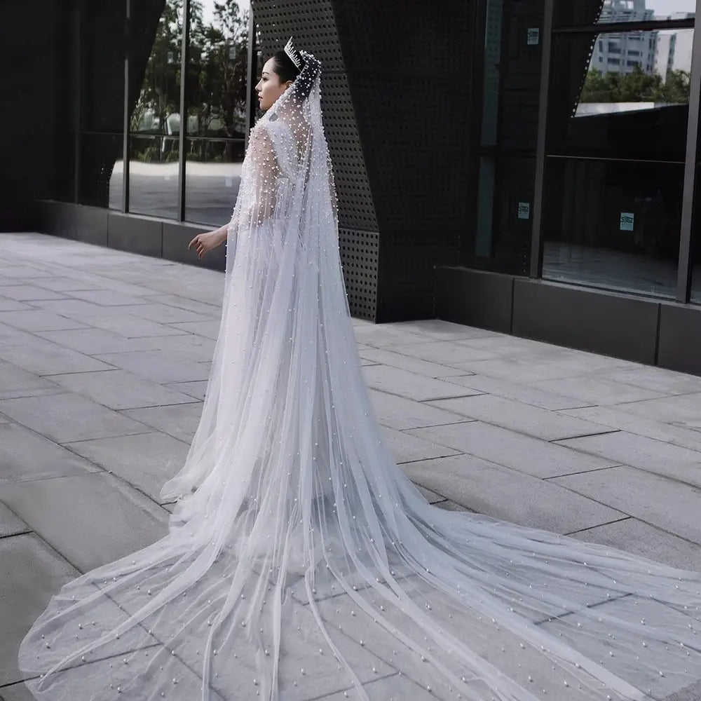A luxury heavy industry bridal pearl veil in white features a long flowing design with delicate beading and a sparkling tiara.