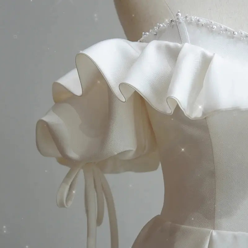 a delicate off the shoulder satin light wedding dress with white ruffle sleeves and subtle beading along the shoulder strap suitable for a wedding dress bride