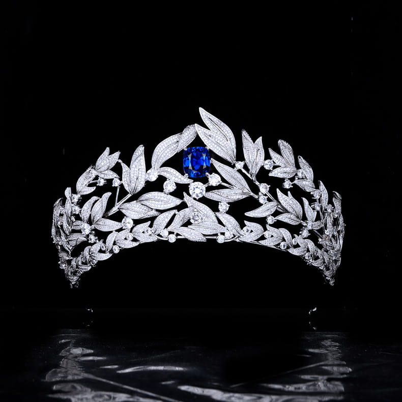 a sparkling silver tiara featuring a sapphire crown copper micro design with intricate leaf and berry motifs and a central deep blue sapphire surrounded by smaller diamonds